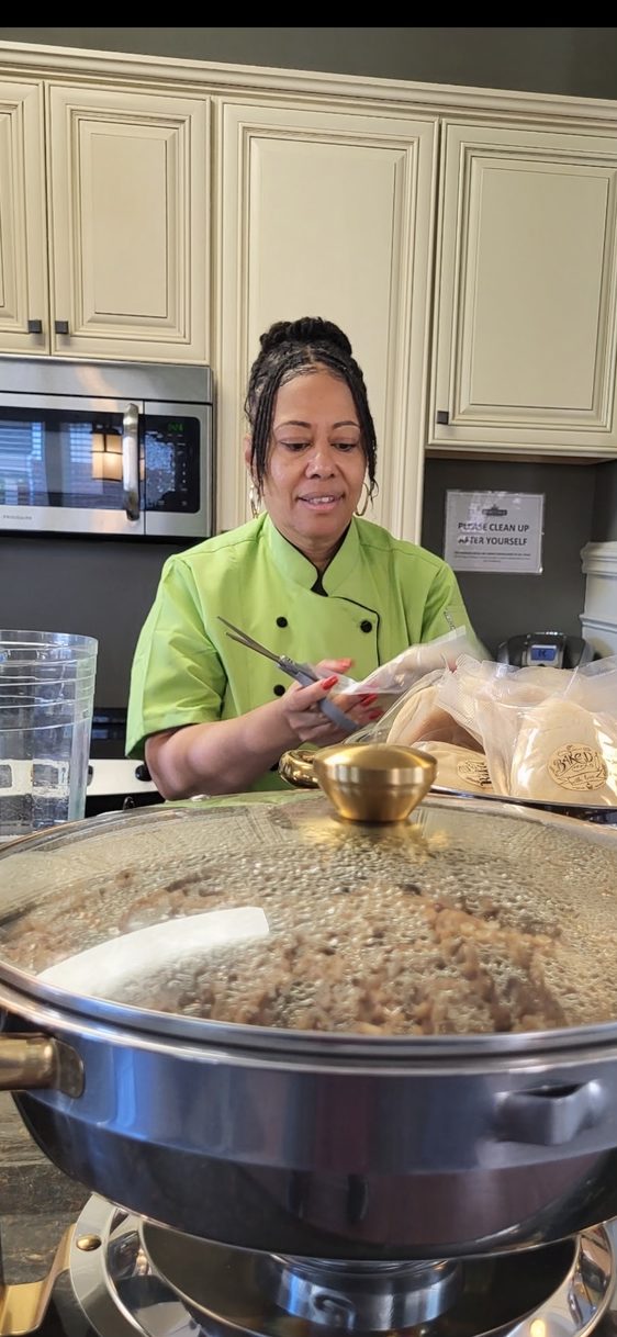 Chef Andrea in her green chef coat, preparing food behind a chafing dish